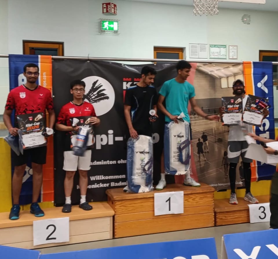 Fünf Spieler mit Urkunden und verpackten Preisen auf dem Podest, rechts reicht eine Person weitere Urkunden an.