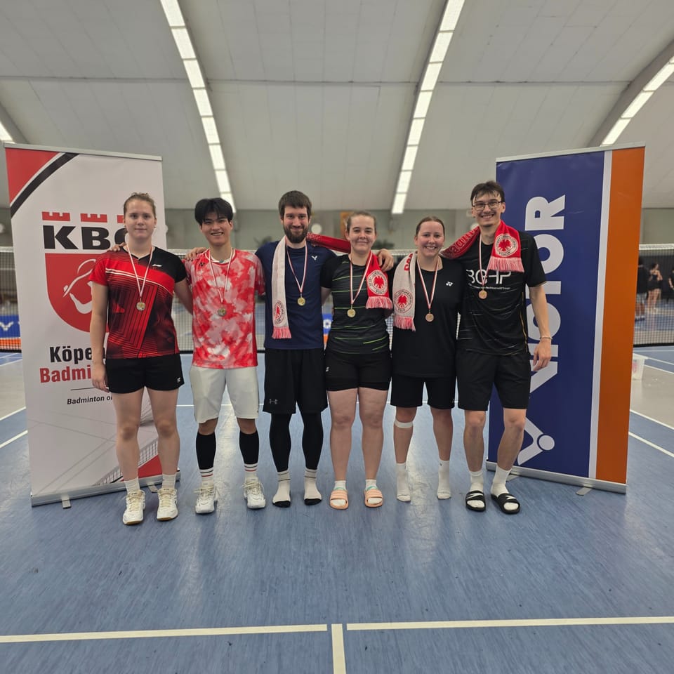 Sechs Badmintonspielerinnen und -spieler mit Medaillen stehen nebeneinander vor einem KBC-Rollup und einem Victor-Banner in der Halle.
