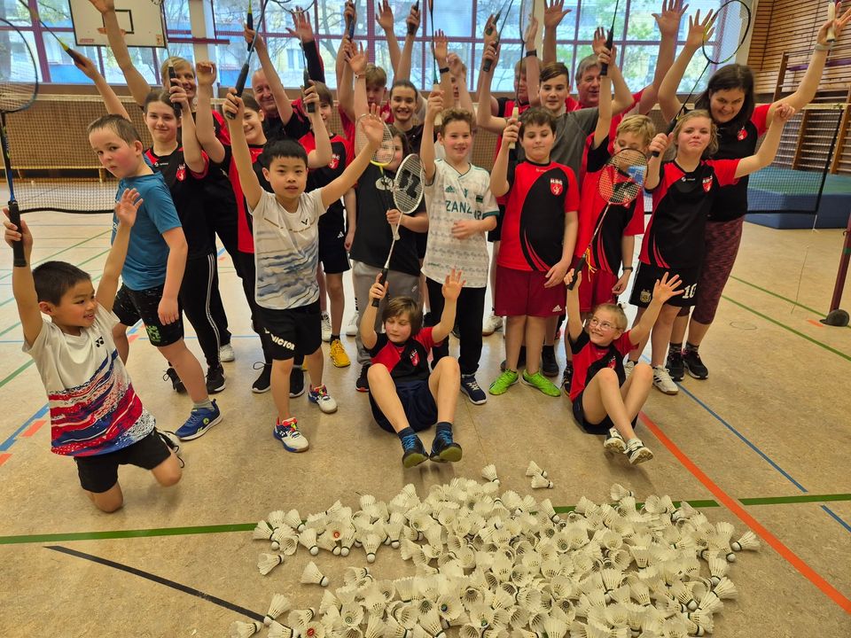 Jubelndes Gruppenfoto des Ostercamps: rund zwanzig Kinder und Jugendliche recken ihre Schläger in die Höhe, davor ein Feld aus Federbällen auf dem Hallenboden