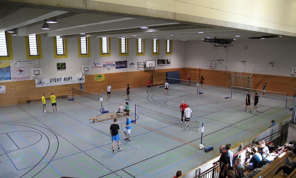 Blick von der Empore auf eine große Sporthalle mit mehreren bespielten Feldern, Anzeigetafel und Zuschauern