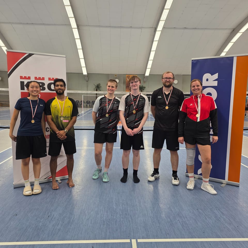 Sechs Medaillengewinnerinnen und -gewinner in Vereinstrikots stehen für ein Gruppenfoto vor dem Netz zwischen den beiden Aufstellern.