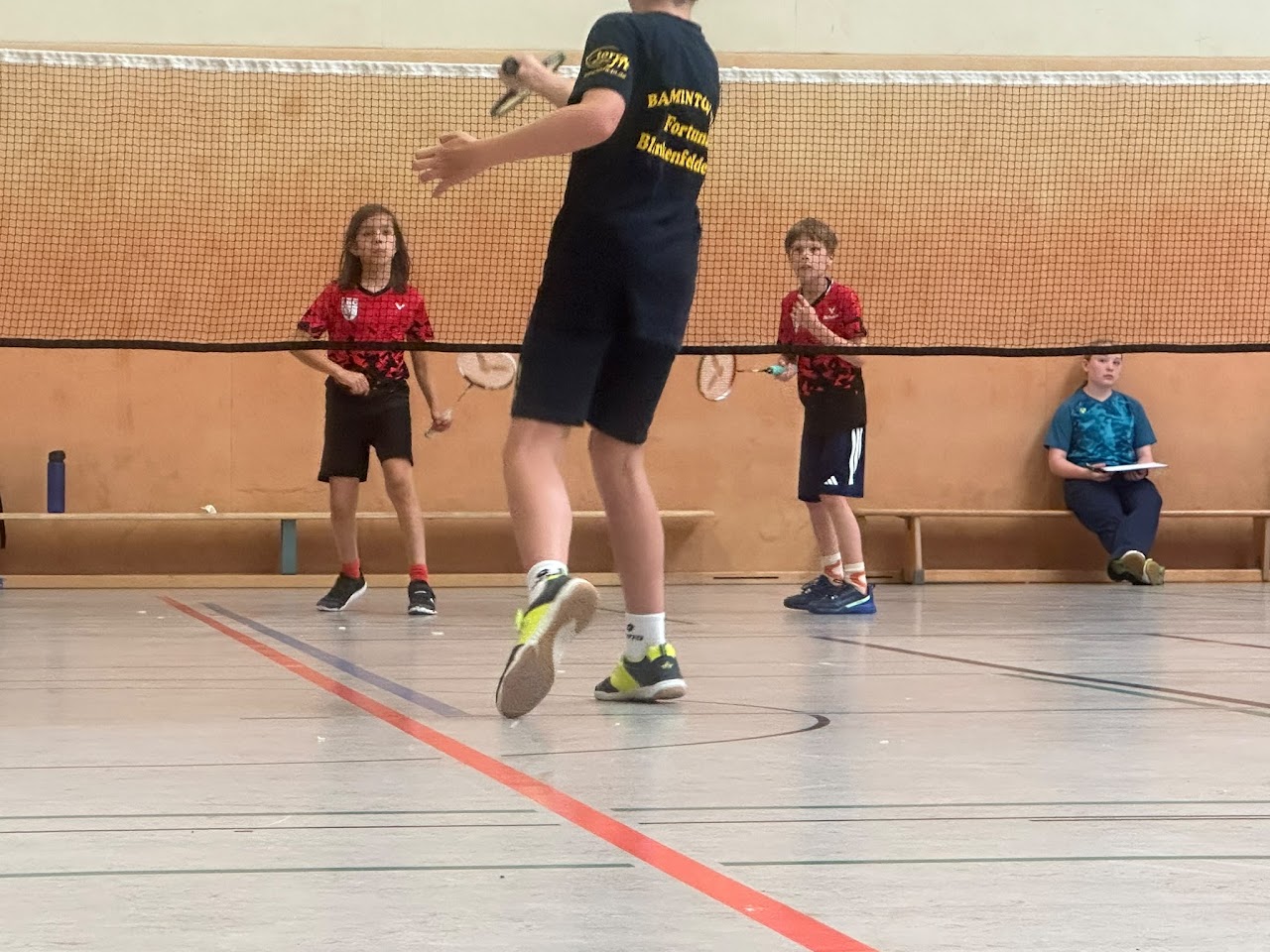 Kinder beim Badmintontraining am Netz mit Trainer